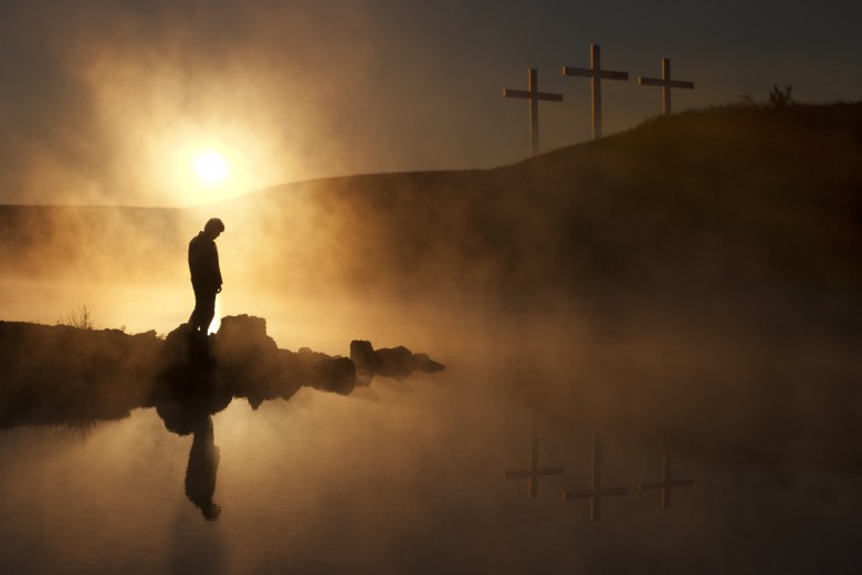 Three Crosses and Silhoutted Person in Prayer at Sunrise